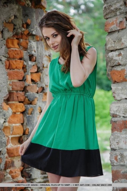 Приятная молодая девушка в зеленом платье фоткается на фоне кирпичной стены с обнаженной вагиной